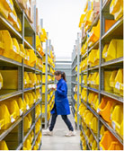 woman in distance wearing blue trench coat walking through aisles containing yellow boxes filled with medical supplies