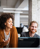 woman of color leaning over bearded man sitting at his desk both smiling
